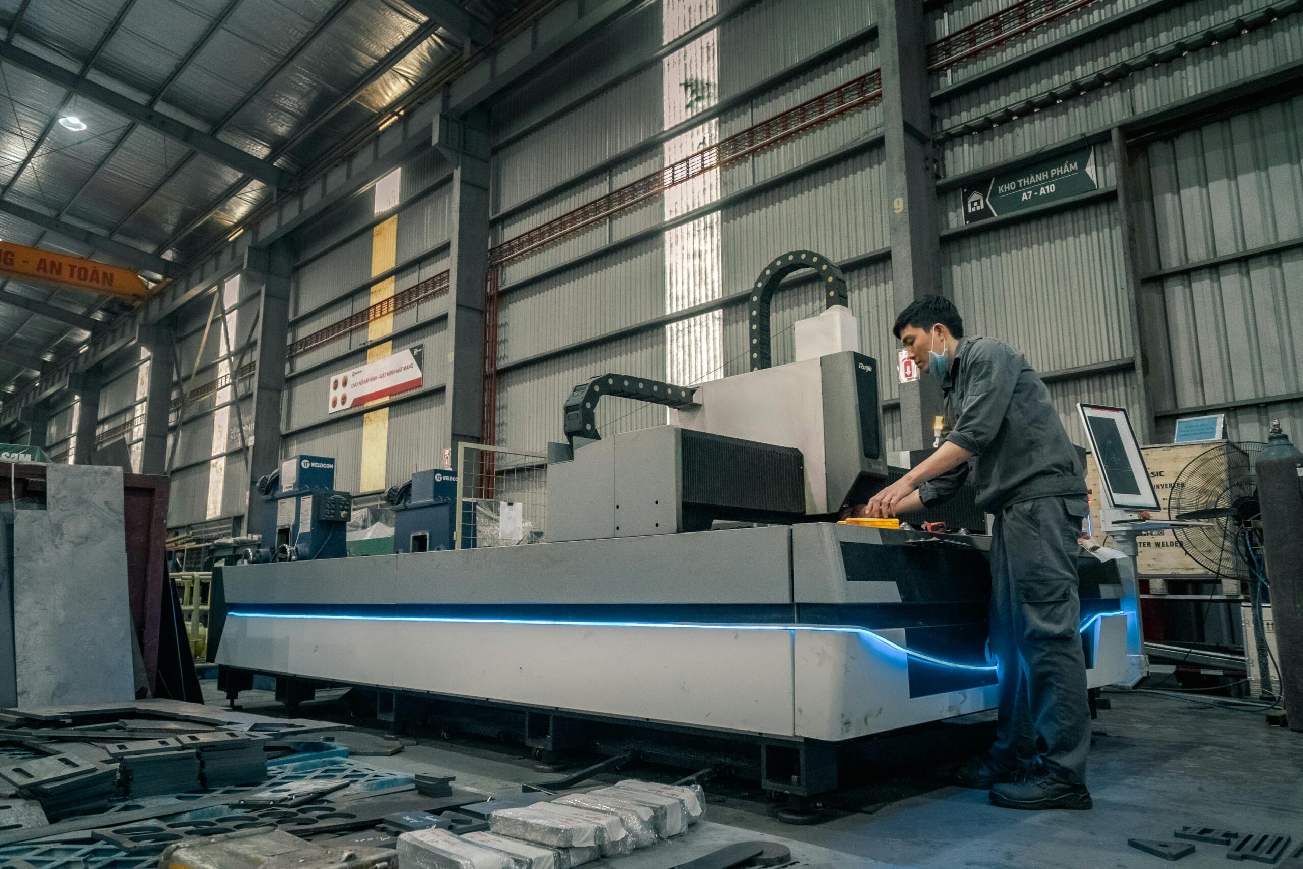 A worker with a mask operating machinery in a spacious industrial warehouse.